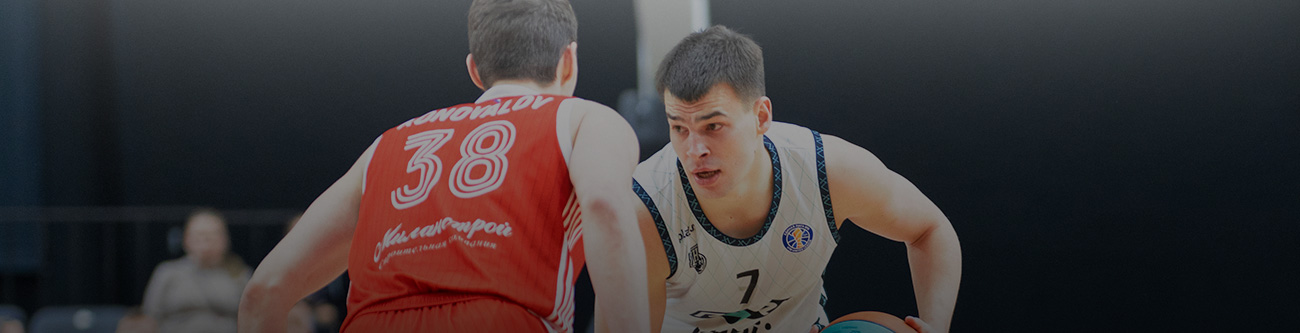 На изображении два баскетболиста на площадке. Один в белой форме с мячом, другой в красной форме, номер 38, готовится защищаться. Оба сосредоточены на игре. Фон размытый